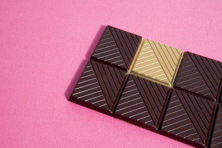 a whole dark chocolate bar with a gold square isolated on a vibrant background. Metaphor of luck. Minimal color still life photography.の写真素材