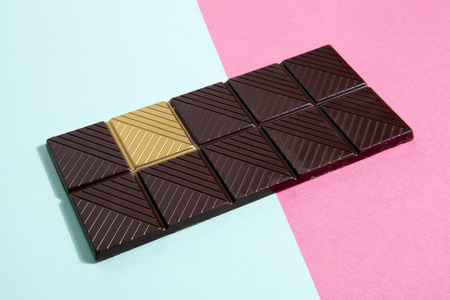 a whole dark chocolate bar with a gold square isolated on a vibrant background. Metaphor of luck. Minimal color still life photography.の写真素材