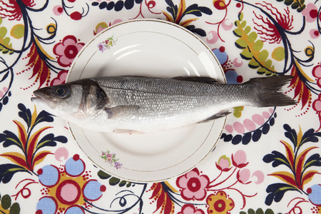 A bass fish inside a flower plate hidden on a flowery fabric. Camouflage game. Minimal color still life photography.の写真素材