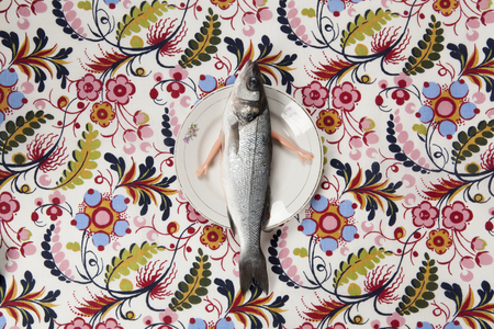 A bass fish with arms doll inside a flower plate hidden on a flowery fabric. Camouflage game and anthropomorphism. Minimal color still life photography.の写真素材