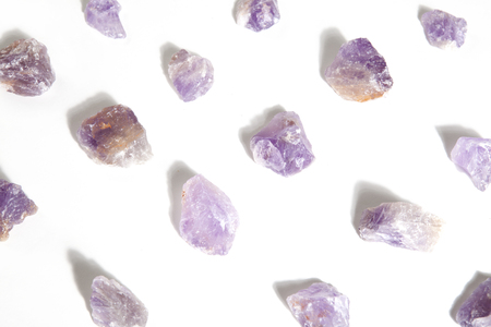 several pieces of raw amethyst lined up on a white background. Minimal color still life photography.