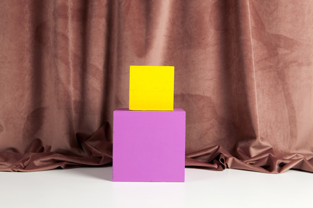Two bright yellow and pink cubes placed one on the other in front of an old pink velvet curtain. Minimum and geometric still life color photographyの写真素材