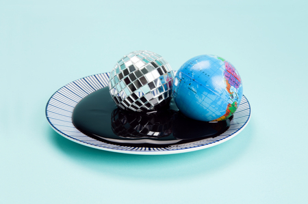 an antistress ball representing the planet earth near a disco ball drowned in an oil spill. Minimal still life color photography.の写真素材