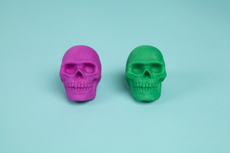 Two plastic skulls, one pink and one green, placed on a turquoise background. Minimal and creative color still life photographyの写真素材