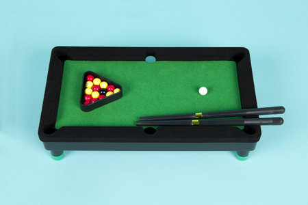a miniature plastic billiard table on a turquoise background, complete with triangle, cues and ballsの写真素材