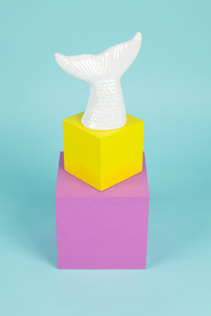 a mermaid tail in iridescent ceramic on a stack of pink and yellow cubes. Turquoise background. Minimal and creative still life photographyの写真素材