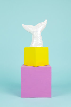 a mermaid tail in iridescent ceramic on a stack of pink and yellow cubes. Turquoise background. Minimal and creative still life photographyの写真素材