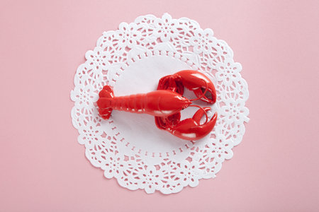 a red metal lobster on a white doily and pink background. minimal color still life photographyの写真素材