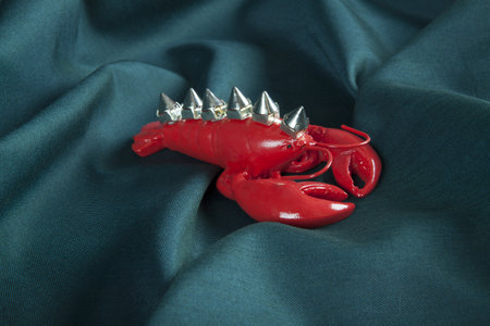 a punk style lobster wearing riveted spikes like a mohican on a green wavy fabric background. Minimal color still life photography.の写真素材
