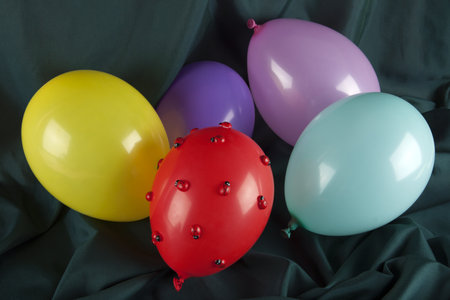 a red balloon covered with ladybugs among balloons in harmonious colors on a wavy green background. Minimal color still life photography.の写真素材