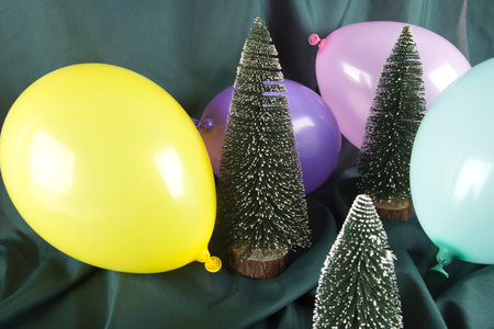 a composition of snowy Christmas trees surrounded by multicolored balloons on a wavy green background. Minimal color still life photography.の写真素材