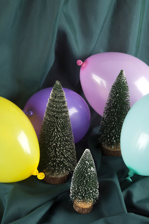 a composition of snowy Christmas trees surrounded by multicolored balloons on a wavy green background. Minimal color still life photography.の写真素材