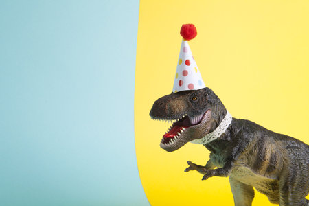 a dinosaur, dressed up in lace and a paper party hat, at a birthday party against a yellow and blue background. Minimal creative still life colorful photographyの写真素材