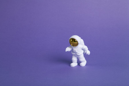 an astronaut figurine in a spacesuit exploring a plain purple background. Minimal creative still...