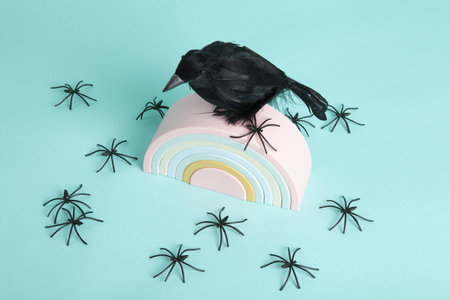 a beautiful raven taking pride of place on plastic rainbow surrounded by an invasion of spiders on a turquoise background. Minimalist, trendy still life photography.の写真素材
