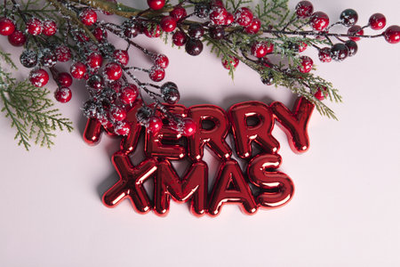 A glossy red plastic Christmas ornament featuring a text saying merry xmas. A branch of holly with its red berries framing the top of the photo. Minimalist, trendy still life photography.の写真素材