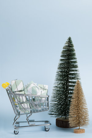 Set with a caddy filled with gifts against a luminous sky-blue background, as well as gold and green Christmas trees. Minimalist, trendy still life photography.の写真素材
