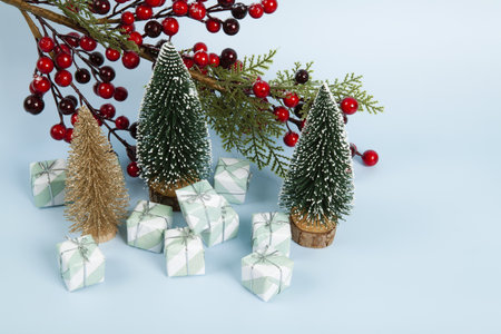 Composition with colorful gifts, a branch of holly with its red berries and christmas tree against a luminous sky-blue background. Minimalist, trendy still life photography.の写真素材