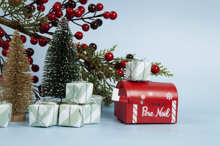 Composition with many gifts, a branch of holly with its red berries, a santa claus mailbox and christmas tree against a luminous sky-blue background. Minimalist, trendy still life photography.の写真素材