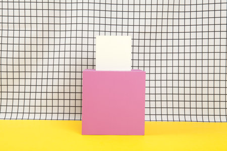 a yellow cube on top of a larger pink cube balanced on a black and white grid background. empty...
