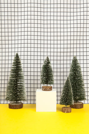 a white wooden cube surrounded by several miniature christmas trees on a black and white grid background. empty object display stand. Minimal still life photographyの写真素材