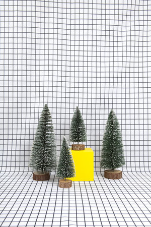 a miniature forest scene composed of several small christmas trees and a yellow cube on a graphic black and white grid background. minimal still life photographyの写真素材