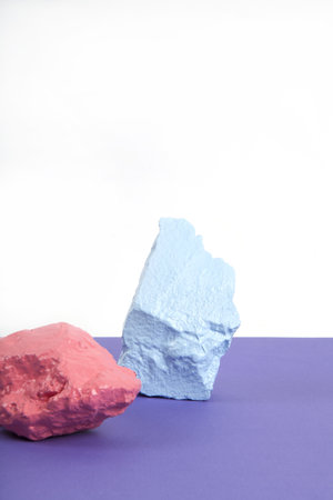 3 paint stones or pebbles in pink, salmon and blue pastel shades isolated on a white and violet background. Minimal still life and vibrant photographyの写真素材