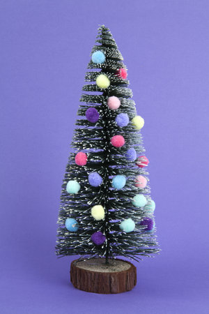 miniature christmas tree decorated with mini garlands and pompoms as baubles. Purple background. Minimal still life photographyの写真素材
