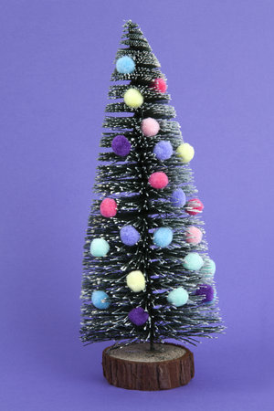 miniature christmas tree decorated with mini garlands and pompoms as baubles. Purple background. Minimal still life photographyの写真素材