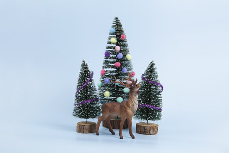 miniature christmas tree decorated with mini garlands and pompoms as baubles. a deer figurine in front of a miniature forest. Blue background. Minimal still life photographyの写真素材
