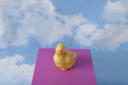 a plaster duck on a pink cube in front of a blue sky with clouds.Minimal still life photographyの写真素材