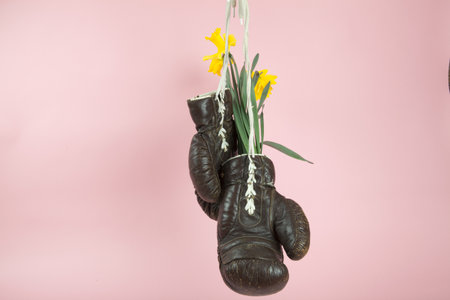 a pair of old boxing gloves hacked to become a vase with narcissus flowers inside hung in front of a...