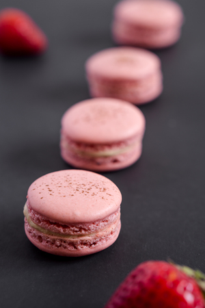 Strawberry macarons on a dark background. Macarons are delicate french pastries consisting of two round meringue cookies and a sweet filling in the center. Light & crisp, these are the perfect luxurious dessert.の写真素材