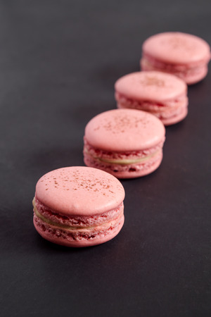 Strawberry macarons on a dark background. Macarons are delicate french pastries consisting of two round meringue cookies and a sweet filling in the center. Light & crisp, these are the perfect luxurious dessert.の写真素材
