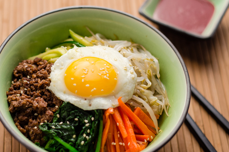 Bibimbap is a classic Korean meal. A bowl of rice is topped with seasoned vegetables, meat and a sunny side up fried egg on top. Spicy chili sauce can be added to finish off this savoury Asian dish.の写真素材