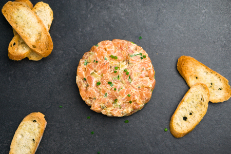 Salmon tartare top view, a dish made with chopped fresh raw salmon fish, avocado, tartar sauce and crackers or bread. This healthy dish is often served as appetizer in fine dining restaurants.の写真素材