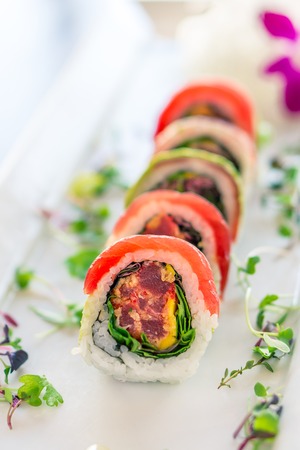 Fresh maguro maki sushi roll. A uramaki style sushi roll on a white plate. The raw sashimi tuna fish and rice are outside while nori is inside. This delicious meal is served in japanese restaurants.の写真素材