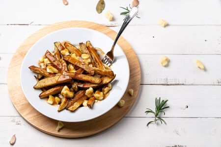 Fast food poutine with fork dug in. A classic fast food cuisine dish from Quebec. This canadian junk food is made with french fries mixed with tasty cheese curds and a delicious brown gravy sauce.の写真素材