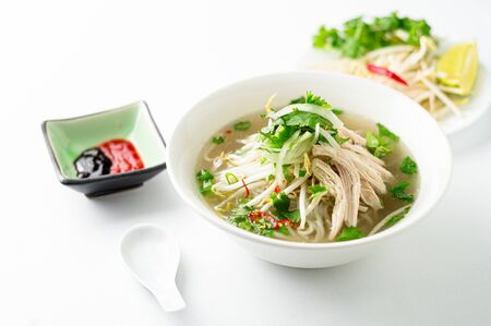 Vietnamese pho soup on white background. A classic authentic vietnamese food, this pho soup is served in a white bowl with chicken broth and lots of fresh garnishes such as cilantro and bean sprouts.の写真素材