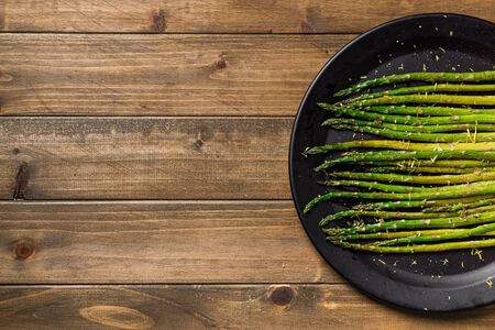 Asparagus on wooden background. Eating healthy food is easy with this homemade vegan dish; roasted asparagus with lemon zest on top. The veggies are served on black plate with wooden table background.の写真素材