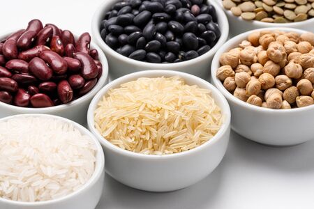 Rice and beans ingredients closeup. Bowl of basmati rice surrounded by other varieties of grains and legumes, such as: chickpeas, red kidney beans, green lentils, black turtle beans and jasmine rice.の写真素材
