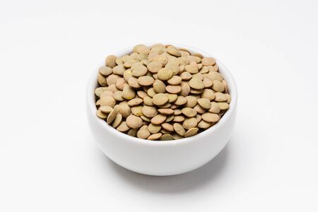 Green lentils bowl on white background. These uncooked green lentils are common staple food ingredients. Also called pulses (dry edible seeds of plants), they are part of the legume family.の写真素材