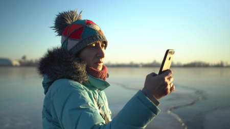 Adult caucasian woman in blue jacket and hat in winter standing on ice