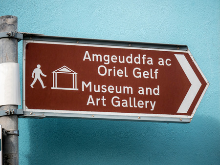 Bilingual tourist sign in Welsh and English giving directions to museum and art gallery in a Welsh town.の写真素材