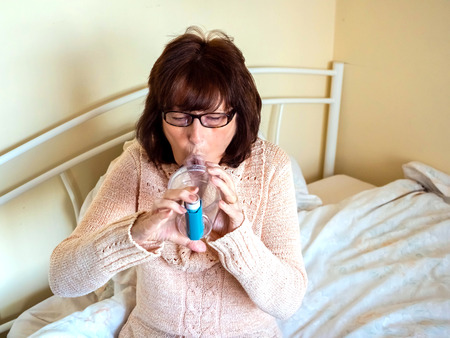 Mature lady using asthma pump spacer device, front view