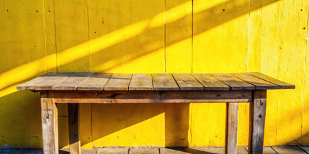Wooden table and chair in front of yellow wooden wall with shadowの素材
