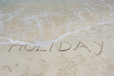 The word Holiday written on the sand of a tropical beach, washed away by the sea. Concept of a holiday endingの写真素材