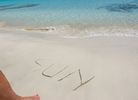 SUN written on the sand of a tropical beach with a foot pointing towardsの写真素材
