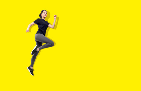 Young fitness woman in sportswear jumping in the air. Over bright yellow background.