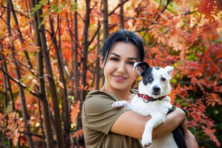 Woman holding a dog in her arms over autumn nature background. lifestyle photo.の写真素材